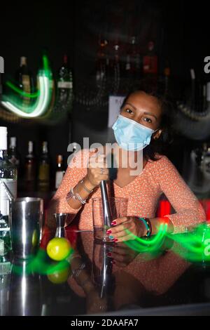 Portrait d'une serveuse exotique avec masque facial préparant un cocktail au bar disco. Flou de mouvement. Espace pour le texte. Banque D'Images