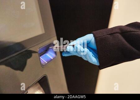 La main dans des gants jetables met la carte bancaire dans ATM pendant Pandémie Covid-19 Banque D'Images