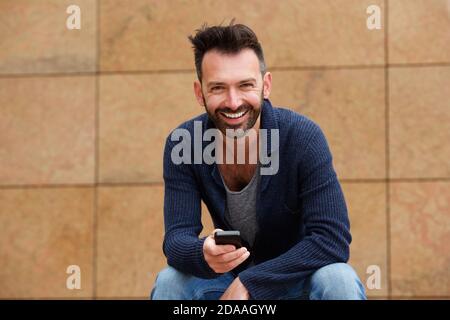 Portrait d'un homme mûr et gai assis à l'extérieur avec un téléphone portable Banque D'Images