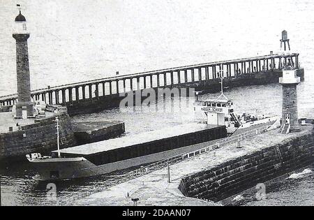 Une photo historique de L'UNION PLUTON , l'un des derniers navires à conteneurs à passer entre les jetées victoriennes et les phares à Whitby, dans le Yorkshire, au Royaume-Uni, peu avant la fin du commerce de fret. Le cargo Union Pluton de 82.5 mètres de long a été construit en 1984. (Panneau d'appel MJAB). Banque D'Images