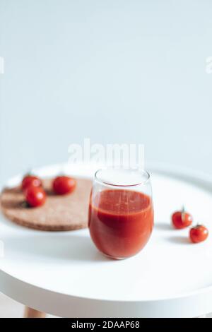 Mini tomates mûres avec un verre de jus de tomate sur une table blanche. Orientation verticale Banque D'Images