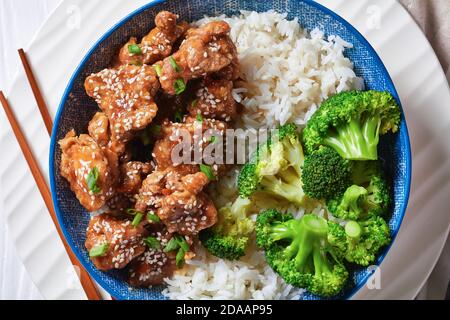 Poulet du général TSO en-cas chinois croustillants dans un bol avec du riz et des bouquets de brocoli à la vapeur, vue horizontale depuis le dessus, plat, macro Banque D'Images