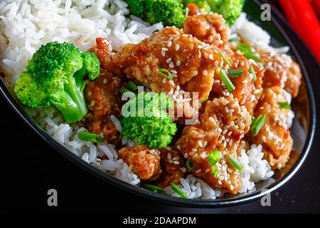 Poulet du général TSO en-cas chinois croustillants dans un bol noir avec du riz et des bouquets de brocoli à la vapeur, vue horizontale d'en haut, gros plan Banque D'Images