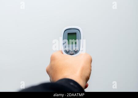 Main du médecin tenant le pistolet thermique sur fond gris. Gros plan d'un thermomètre à aiguille dans un hôpital. Banque D'Images