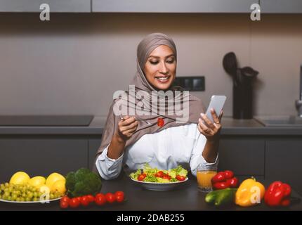 Femme musulmane utilisant un smartphone salade manger déjeuner dans la cuisine Banque D'Images