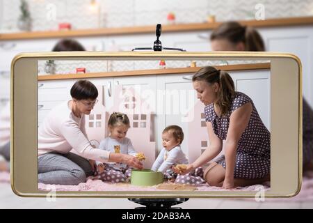 Jeune femme blogueuse en ligne influenceur maman avec grand-mère et deux filles, en streaming en direct un parent jouant avec des enfants spectacle sur les médias sociaux usin Banque D'Images