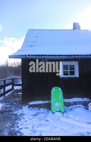 Traîneau en plastique vert sur de la neige fraîche près de la maison rurale mur à la campagne Banque D'Images