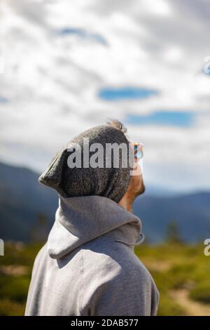 Jeune homme blanc de derrière avec des lunettes de soleil dans beau naturel cadre entouré de montagnes qui surplombent un ciel nuageux Banque D'Images