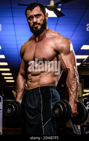 beau jeune homme barbu avec haltères dans le sport éclairé en bleu faites de la gym pendant les entraînements intensifs Banque D'Images