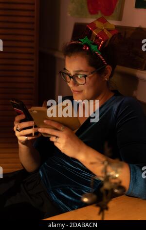 Nerdy jeune femme avec des cheveux décorés regardant accro à deux téléphones cellulaires à Noël. Banque D'Images