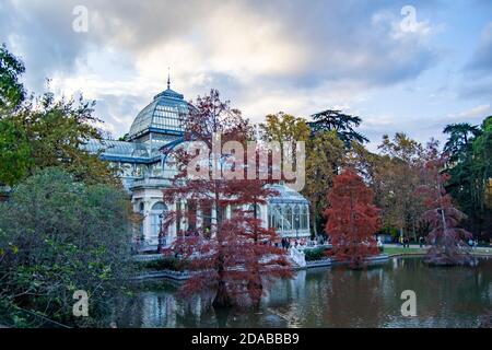 Le Crystal Palace dans le parc Retiro de Madrid avec un paysage automnal et une journée un peu nuageux au coucher du soleil. Arbres aux couleurs d'automne et lumière d'automne. Banque D'Images