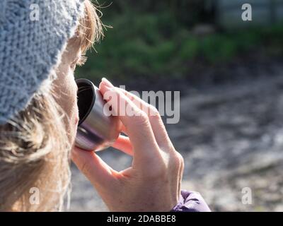 Gros plan d'une dame portant un chapeau de galet avec concentration sur sa boisson d'une tasse d'argent d'une fiole.la lumière du soleil brille sur son visage. Banque D'Images