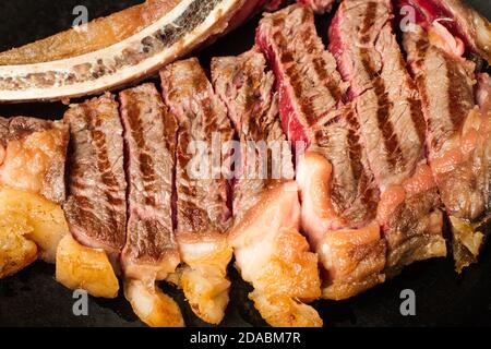 Steak grillé en tranches avec os sur une assiette noire dans vue rapprochée Banque D'Images