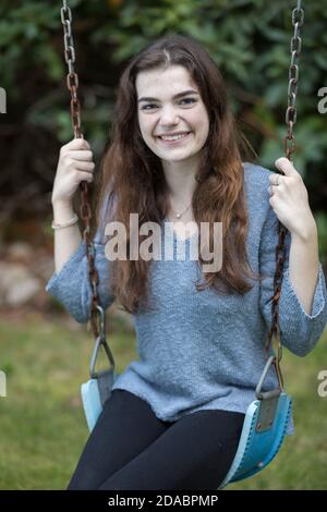 Jolie jeune fille assise sur balançoire souriante avec de la verdure dedans arrière-plan Banque D'Images