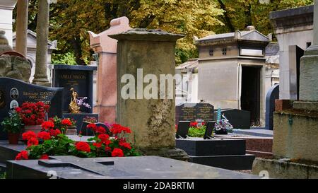 Paris, France - 09/08/2019: Pierres tombales décorées de fleurs sur le cimetière de Montmartre, l'un des plus grands cimetières de Paris, avec des arbres décolorés. Banque D'Images