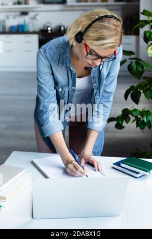 jeune femme blonde en lunettes écrivant des notes dans un carnet Banque D'Images