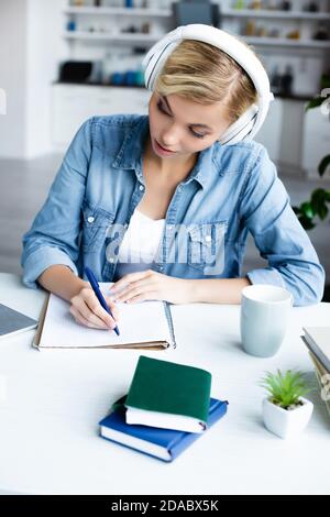 jeune femme blonde dans le casque étudiant en ligne et de prendre des notes Banque D'Images