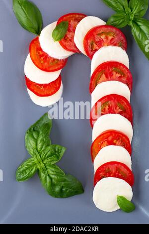 Salade de cape de Noël sous forme de canne à sucre. Mozzarella et tomate sur plaque grise servies pour le nouvel an en arrière-plan Banque D'Images