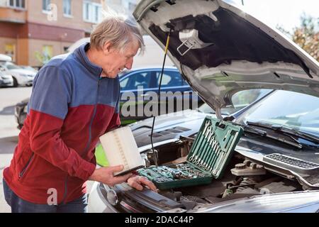 Un conducteur senior qui cherche un moteur de voiture à trouver une boîte à air pour la nouvelle cartouche d'air propre. Vus avec capot ouvert Banque D'Images