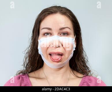 Dégoût sur le visage d'une femme, la bouche ouverte et la langue adhérant sous un masque médical. Calme les yeux. Supposition d'émotions réelles en portant un masque. Portrait sur un Banque D'Images