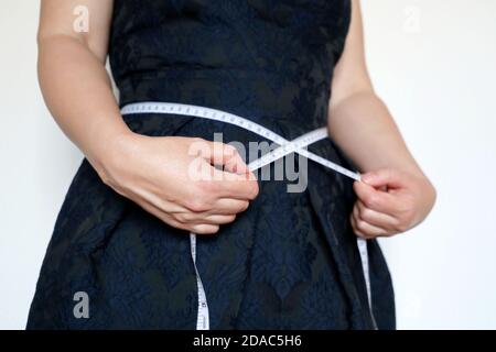 Perte de poids, amincissement, concept de régime. Femme en robe bleu foncé debout avec du ruban de mesure autour de la taille Banque D'Images