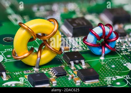 Deux inductances toroïdales et transistors électroniques sur une carte de circuit imprimé verte. Belle bobine d'induction jaune ou bleue sur ci dans convertisseur de tension intégré. Banque D'Images