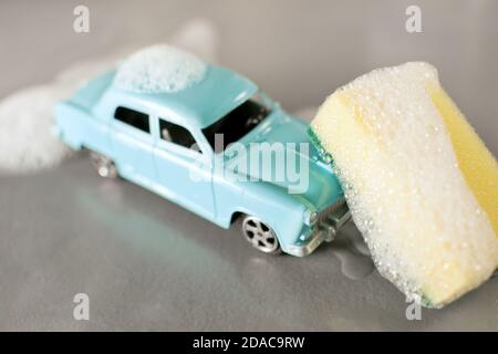 Scène de lavage de voiture avec petit modèle de production de masse de jouet soviétique populaire d'époque Volga GAZ-21, éponge jaune, mousse autour sur fond gris. Banque D'Images