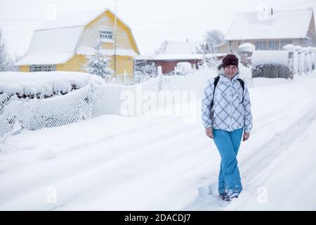 Portrait de femme caucasienne adulte debout sur une route enneigée dans un village pendant une forte chute de neige, un randonneur avec sac à dos Banque D'Images