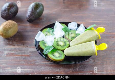 Sorbet sain fait maison (crème glacée aux fruits) fait d'avocat et de kiwi sur l'assiette noire parmi des morceaux de kiwi, feuilles de menthe, cubes de glace sur l'ancienne table Banque D'Images