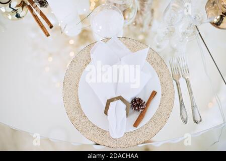 Table en verre festive du nouvel an. Carte de vœux. Dans les branches de l'arbre de Noël sont des verres à champagne, des couverts, une assiette avec dorure Banque D'Images