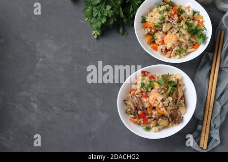 Deux assiettes de riz frit avec fruits de mer, légumes, gingembre et persil sur fond sombre. Cuisine asiatique. Plats végétariens. Vue de dessus. Copier l'espace Banque D'Images