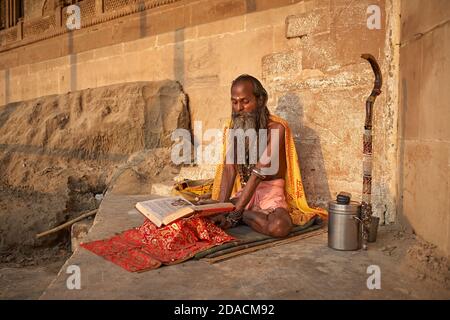 Varanasi, Inde, octobre 2011. Un Sadhu lit un livre Saint dans un ghat sur le Gange. Banque D'Images