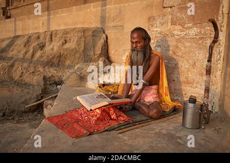 Varanasi, Inde, octobre 2011. Un Sadhu lit un livre Saint dans un ghat sur le Gange. Banque D'Images