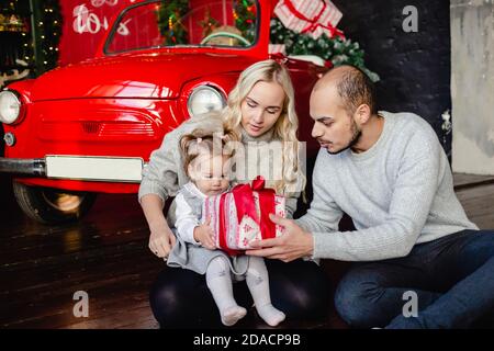 Famille heureuse avec petite fille s'amuser à la maison. Parents donnant un cadeau de Noël à l'enfant. Famille aimante avec des cadeaux dans la chambre. Banque D'Images