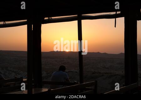 Silhouette de l'arrière d'un homme relaxant et regardant le coucher du soleil avec une bouteille de bière au point de vue Panorama de Red Valley, Cappadoce, Turquie Banque D'Images