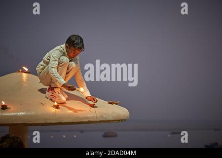 Varanasi, Inde, novembre 2015. Un garçon éclaire des bougies dans un ghat sur le fleuve Ganges la nuit. Banque D'Images