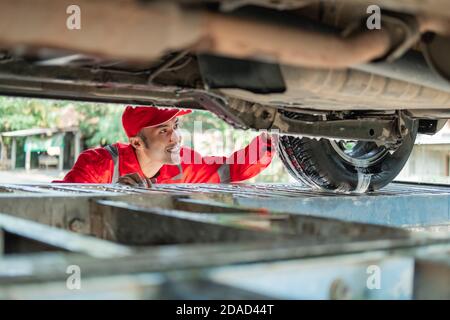 le nettoyant automobile pour homme portant l'uniforme rouge se présente sous le voiture pendant le lavage de la voiture dans le salon de voiture Banque D'Images