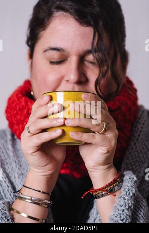 Image verticale d'une femme qui boit du thé dans une tasse jaune. Elle se réchauffe avoir quelque chose de chaud. Concept d'hiver Banque D'Images