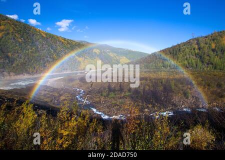 Un bel arc-en-ciel lumineux en pleine taille sur fond de collines d'automne et d'un petit ruisseau. Banque D'Images