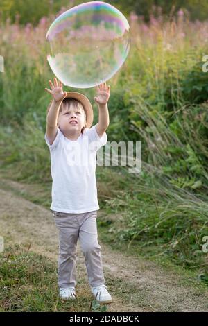 Joyeux garçon attrapant des bulles de savon dans la nature en été Banque D'Images