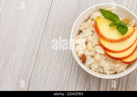 Bol en porcelaine avec porridge au sorgho, pêches coupées, noix de cajou, amande et feuilles de menthe sur les planches de bois grises. Salade de sorgho végétalienne sans gluten avec Banque D'Images