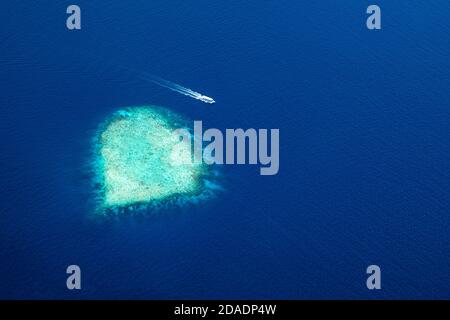 Magnifique récif de corail en forme de coeur, île aux Maldives avec bateau solitaire passant par. Paysage aérien incroyable, paysage marin, destination de voyage exotique Banque D'Images