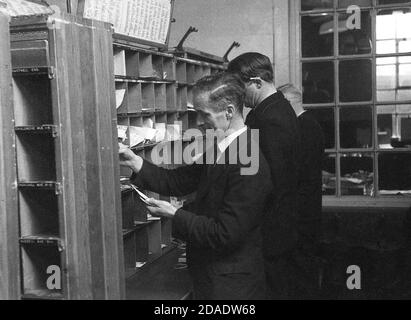 Années 1950, image historique des employés de GPO mettant des lettres ou du courrier dans les trous individuels cuppy sur un côté, Londres, Angleterre, Royaume-Uni. Comme on peut le voir, à cette époque il n'y avait pas de mécanisation et toutes les lettres devaient être triées à la main et sur une unité murale, les lettres seraient mises dans la bonne petite section ou le trou cubby basé sur les zones ou les districts. Banque D'Images