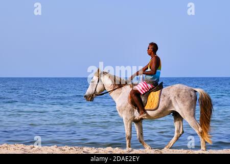 Un homme arabe en lunettes de soleil sur un cheval blanc se déplace le long de la plage. Pilote de mer arabe au Moyen-Orient - Tunisie, Sousse, Afrique 06 13 2019 Banque D'Images