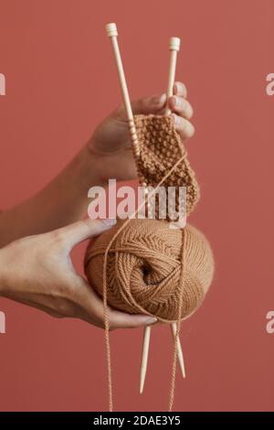 Gros plan de la femme tenant le fil et les aiguilles et tricotage au chaud foulard sur fond rose Banque D'Images