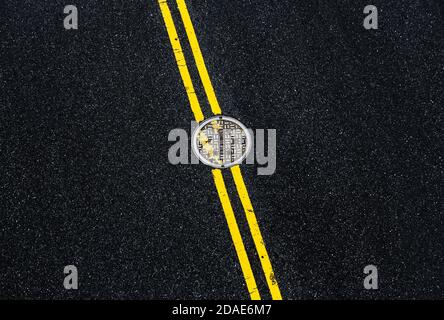 Double ligne jaune continue avec le couvercle de la trappe. Marquages routiers sur asphalte dans la rue de Manhattan à New York. Mots NYC égout sur la crique de la trappe Banque D'Images