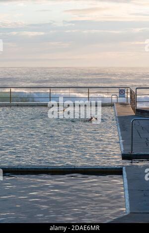 Avec les vagues de l'océan qui se baladent tôt le matin, les nageurs font des longueurs à la Black Head Ocean Pool sur la Barrington Coast, en Nouvelle-Galles du Sud, en Australie Banque D'Images