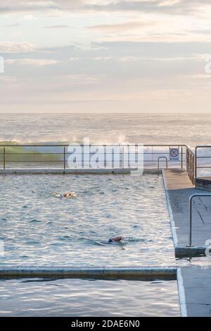 Avec les vagues de l'océan qui se baladent tôt le matin, les nageurs font des longueurs à la Black Head Ocean Pool sur la Barrington Coast, en Nouvelle-Galles du Sud, en Australie Banque D'Images