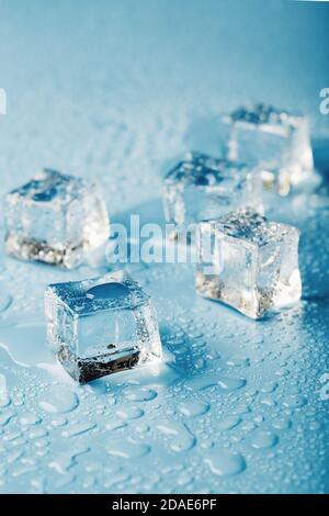 Gros plan sur des glaçons avec gouttes d'eau de fusion dispersées sur un fond bleu. Banque D'Images