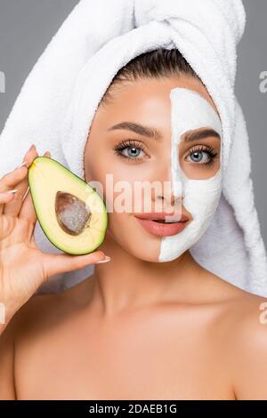 femme avec une serviette sur la tête et un masque en argile sur le visage tenue de l'avocat isolé sur gris Banque D'Images